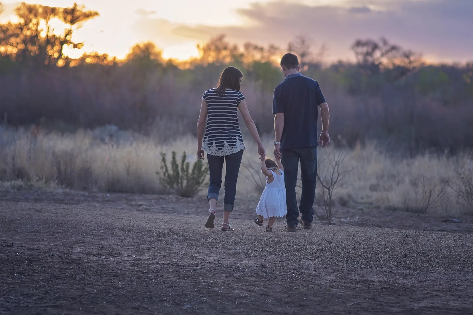 Una familia de espaldas caminando al atardecer, llevando de la mano a su hija pequeña